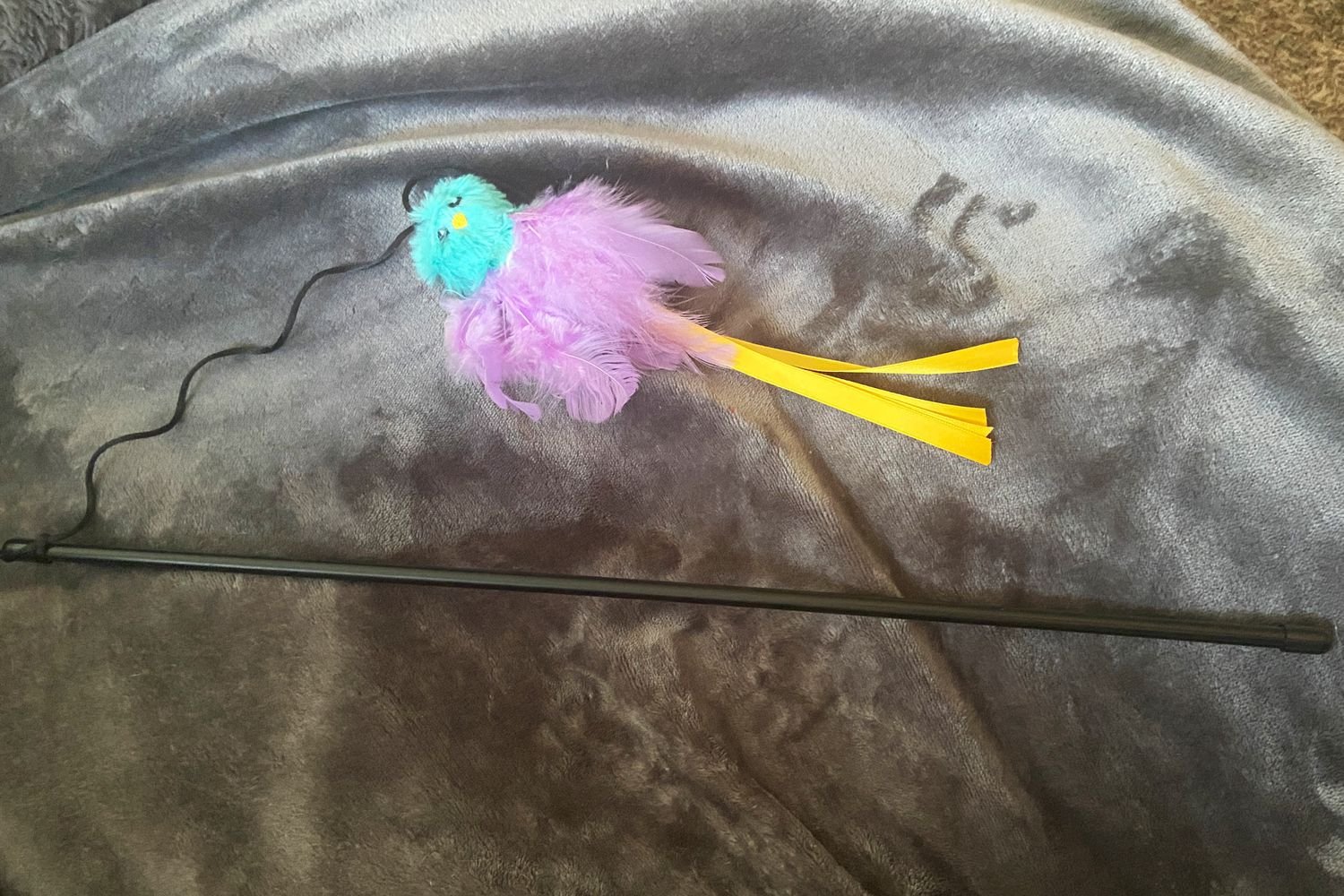 The Frisco Bird with Feathers Teaser Wand Cat Toy with Catnip laying on a blanket