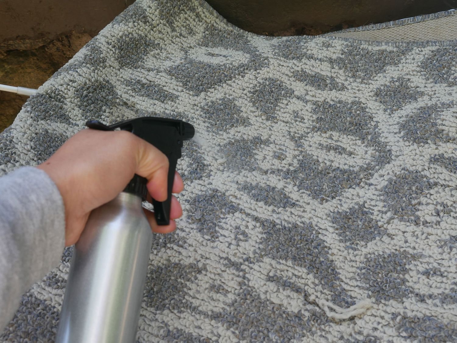 Hand using Bubba's Rowdy Friends Pet Stain & Odor Terminator to spray a patterned rug