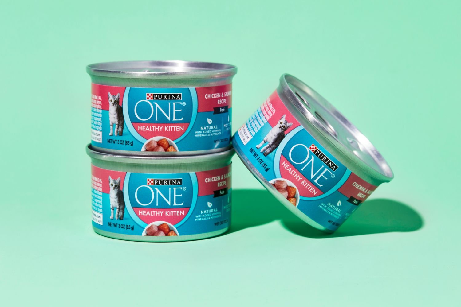 Three stacked cans of Purina ONE Healthy Kitten Wet Food on a green background