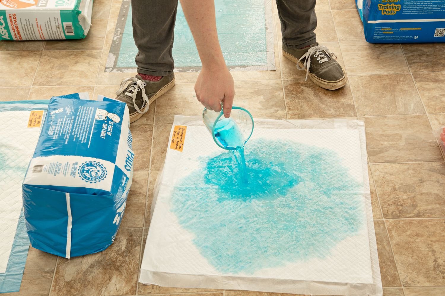 A person pouring a blue liquid on the Bulldogology Puppy Training Pads