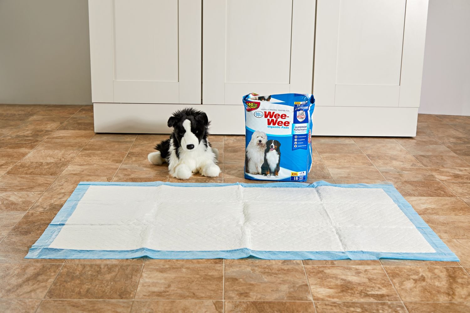 A Wee-Wee Pads Gigantic Dog Pee Pad displayed on a laminate floor in front of a stuffed dog and a box of unopened pee pads