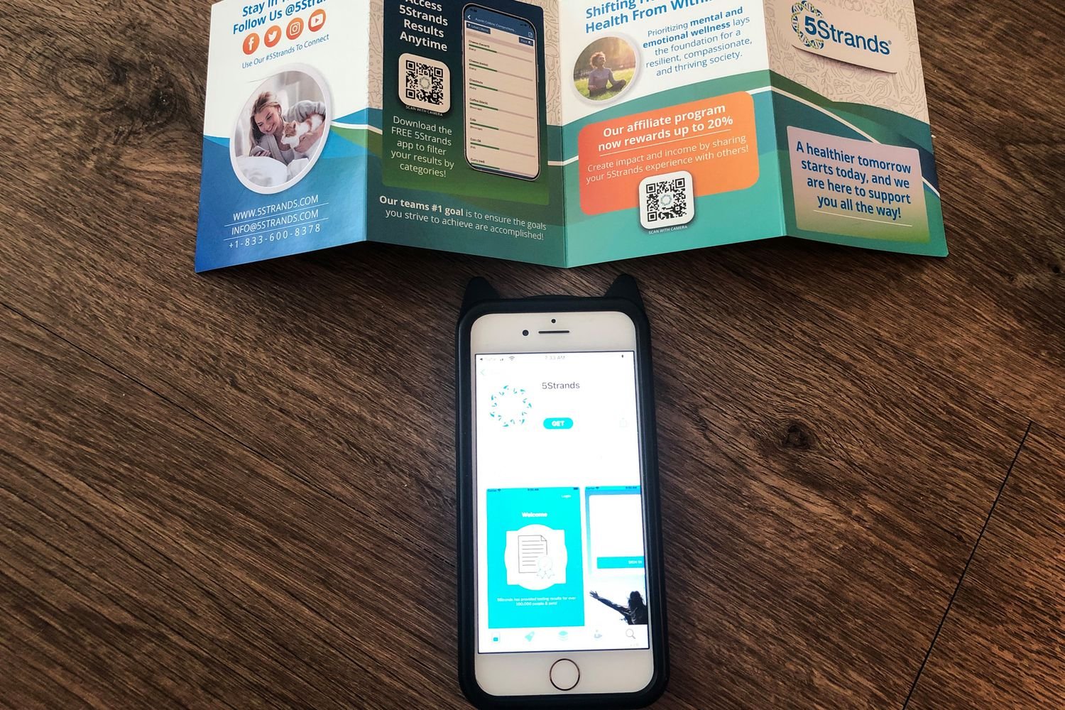 The 5Strands Pet Food & Environmental Intolerance Testing Kit instructions and a phone containing its app on a wooden surface