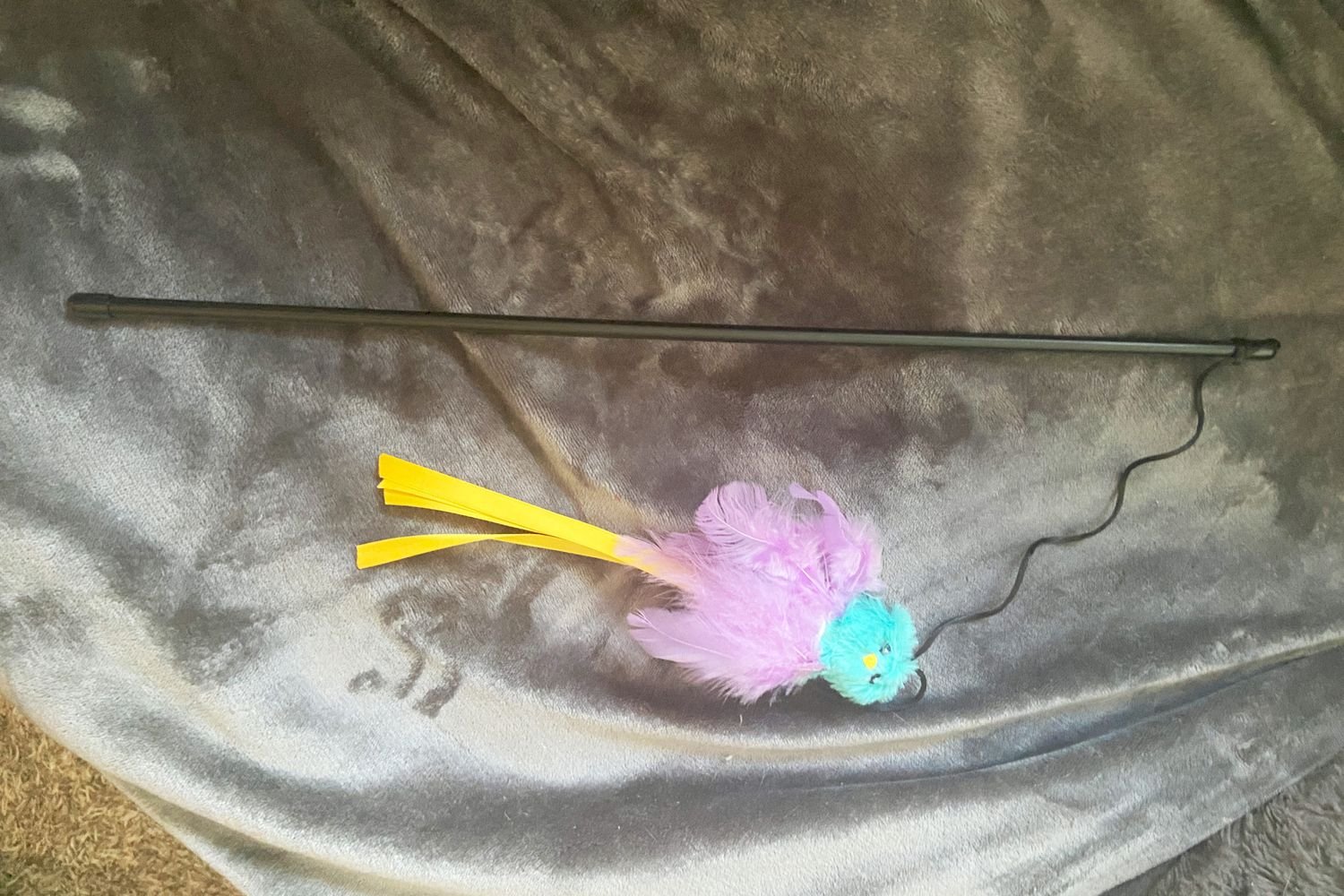 The Frisco Bird with Feathers Teaser Wand Cat Toy with Catnip laying on a blanket